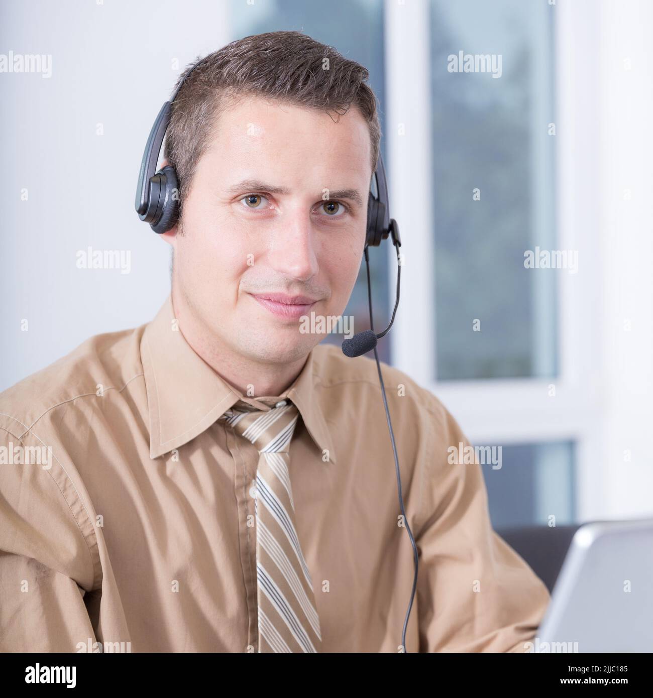 Ein freundlicher Mann mit einem Headset arbeitet im Home Office an einem Computer Stockfoto