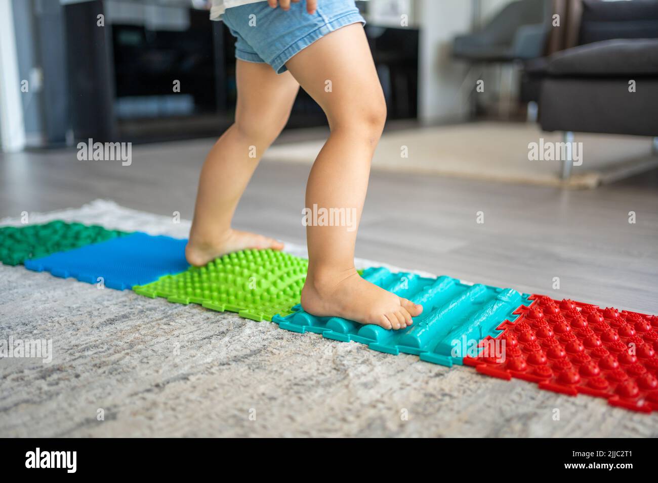 Nahaufnahme eines kleinen Mädchens, das auf einer Massagematte läuft. Babyfußmassagematte für Kleinkinder. Übungen für Beine orthopädische Massage Teppich. Stockfoto