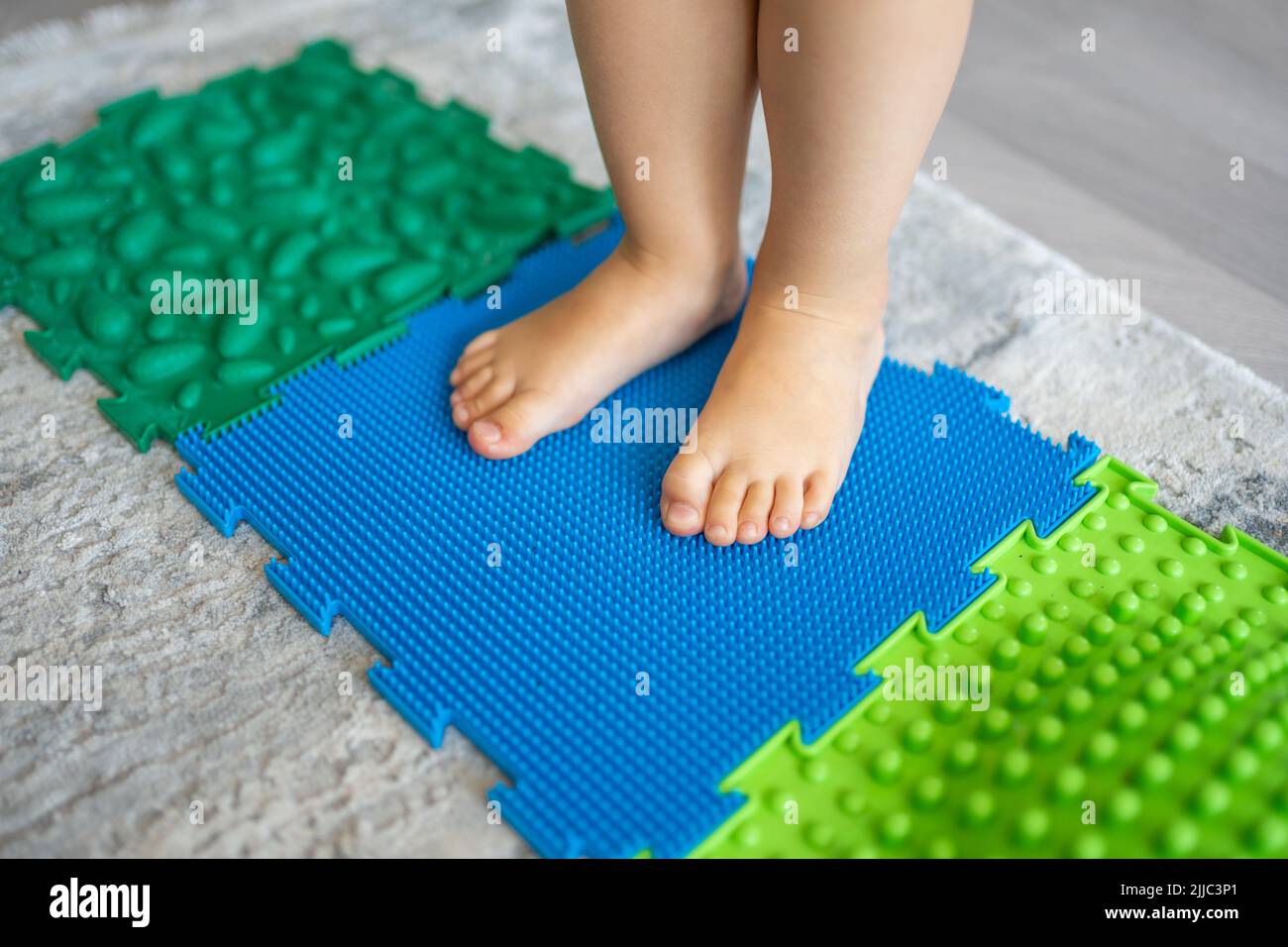 Nahaufnahme eines kleinen Mädchens, das auf einer Massagematte läuft. Babyfußmassagematte für Kleinkinder. Übungen für Beine orthopädische Massage Teppich. Stockfoto