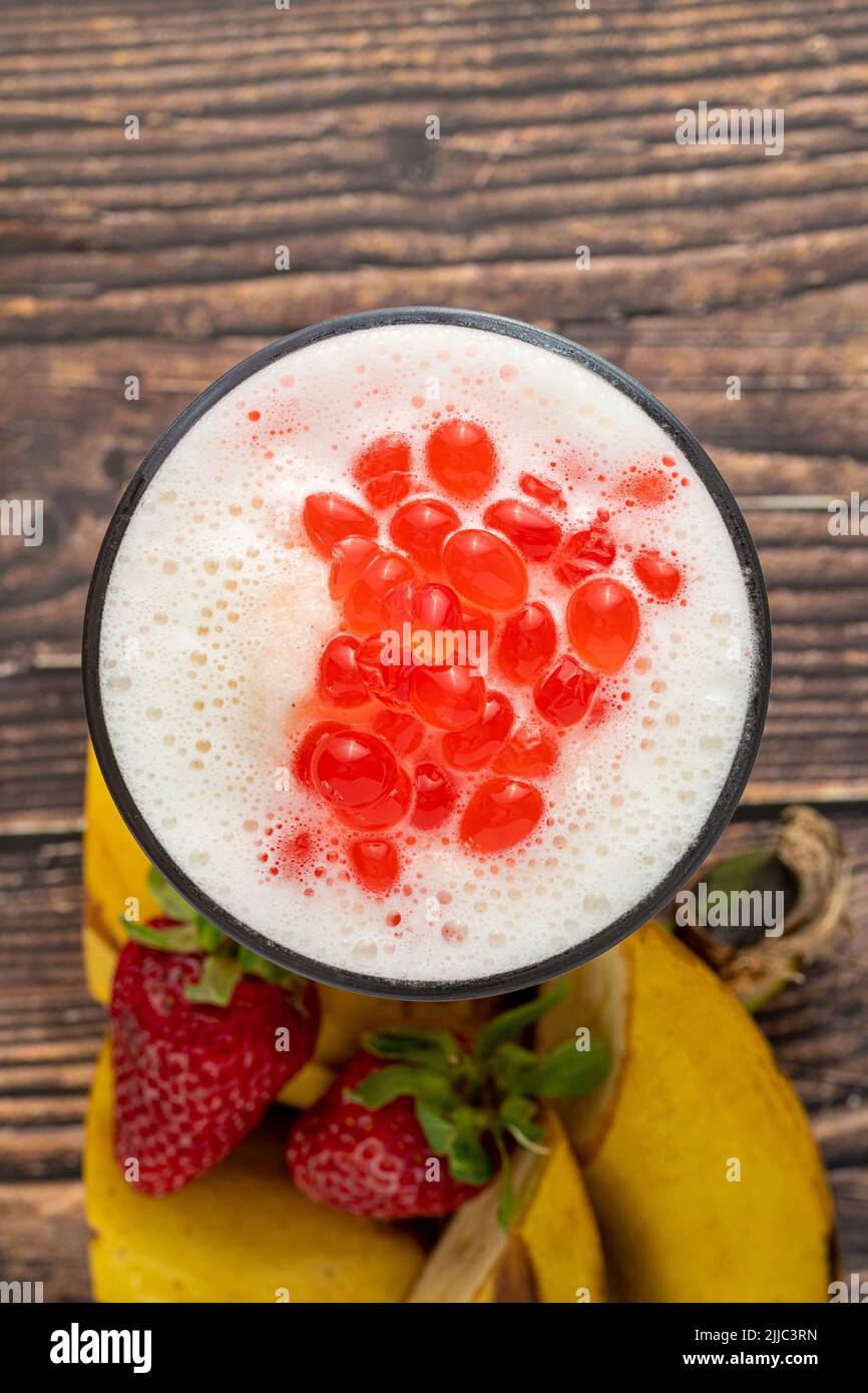 Bananen-, Erdbeer- und Ananas-Smoothie auf dem Holztisch und Bubble Tea oder boba-Teebällchen darauf Stockfoto