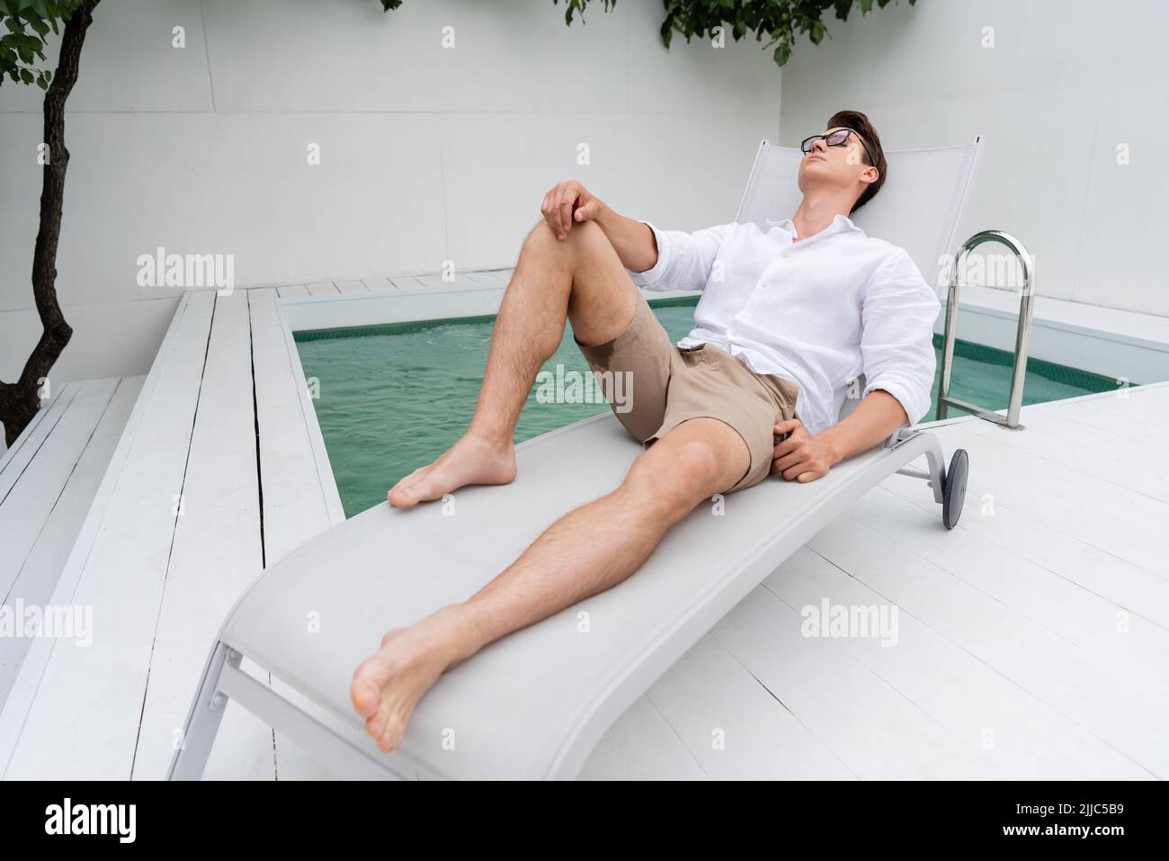 Barfußmann in Sommerkleidung, der sich auf dem Liegestuhl am Pool ausruht Stockfoto