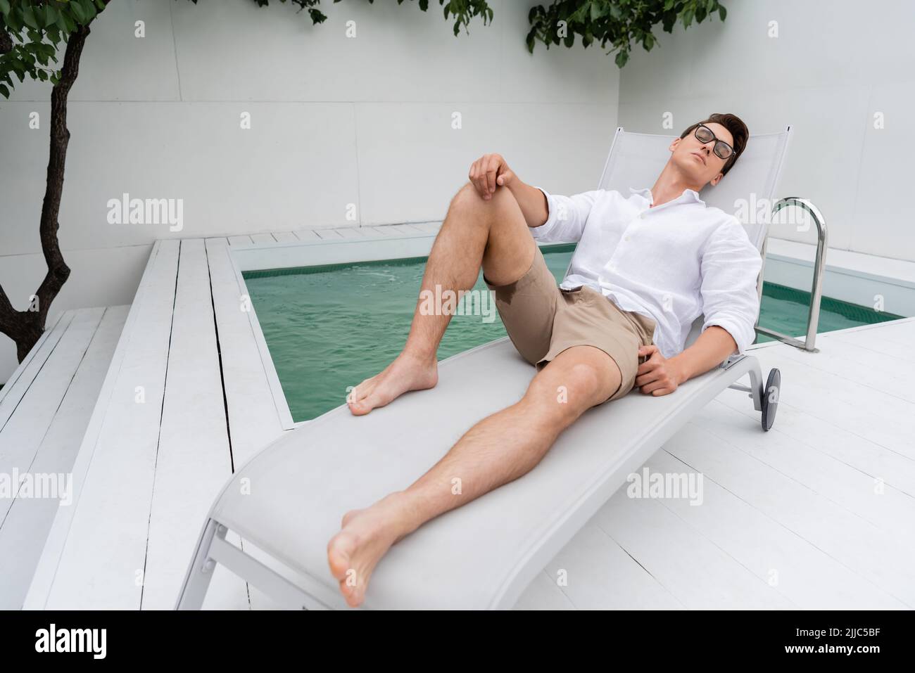 Barfuß Mann in Shorts und Brillen, der auf dem Liegestuhl in der Nähe des Pools liegt Stockfoto