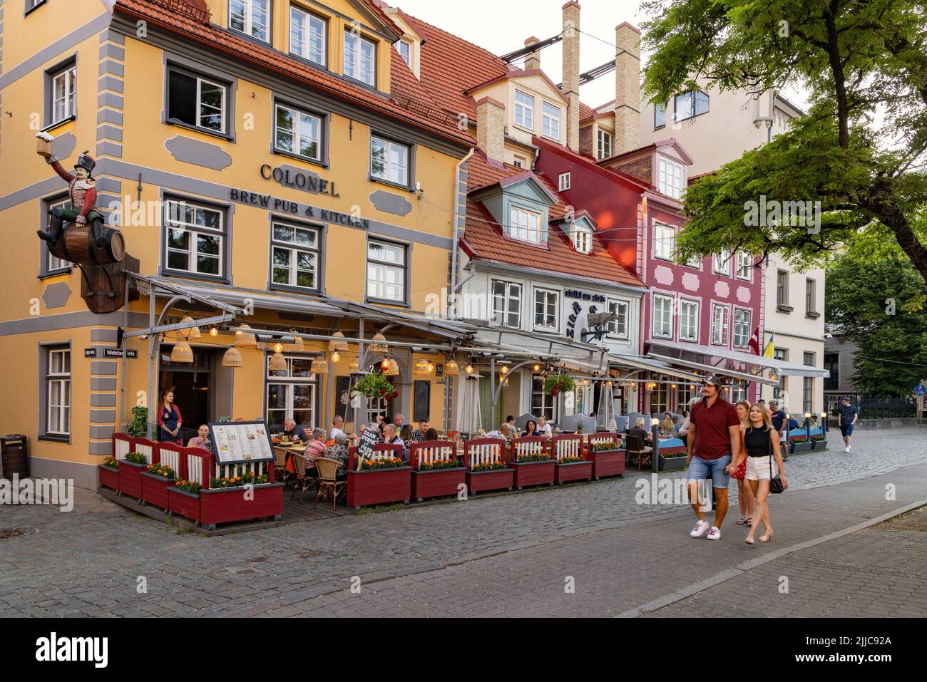 Kneipe und Straßenszene in Riga; Menschen, die am frühen Abend an Pubs und Cafés vorbeilaufen, Altstadt von Riga, Riga Lettland Europa Stockfoto