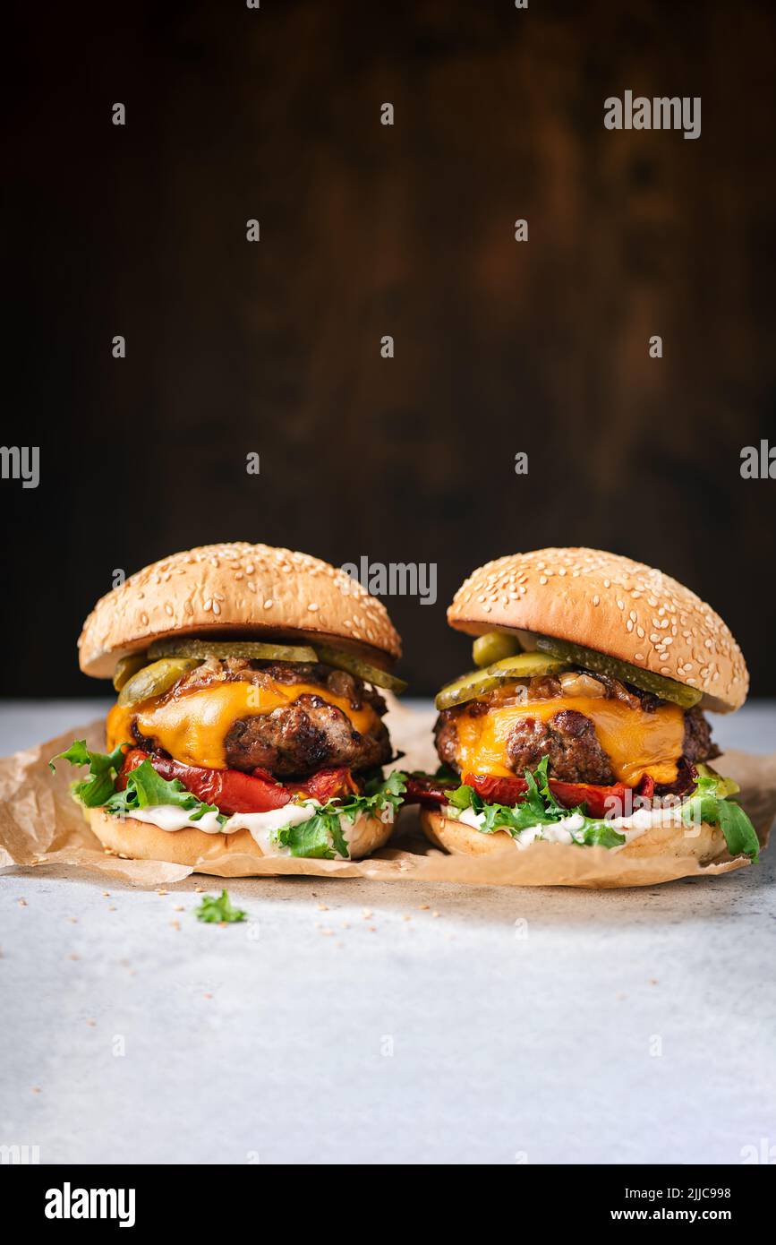 Superleckere, handgefertigte, saftige Cheeseburger mit gegrilltem Paprika, Rucola, Sauce und Gurken auf Holzboden. Platz für Text oder Design e kopieren Stockfoto