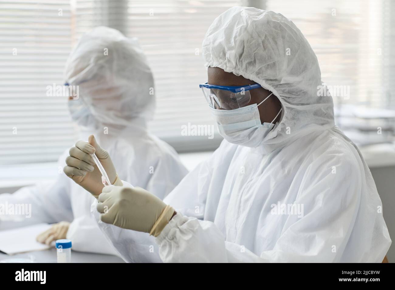 Porträt einer jungen Wissenschaftlerin, die volle Schutzkleidung trägt, während sie im medizinischen Labor mit gefährlichen Proben forscht, Kopierraum Stockfoto