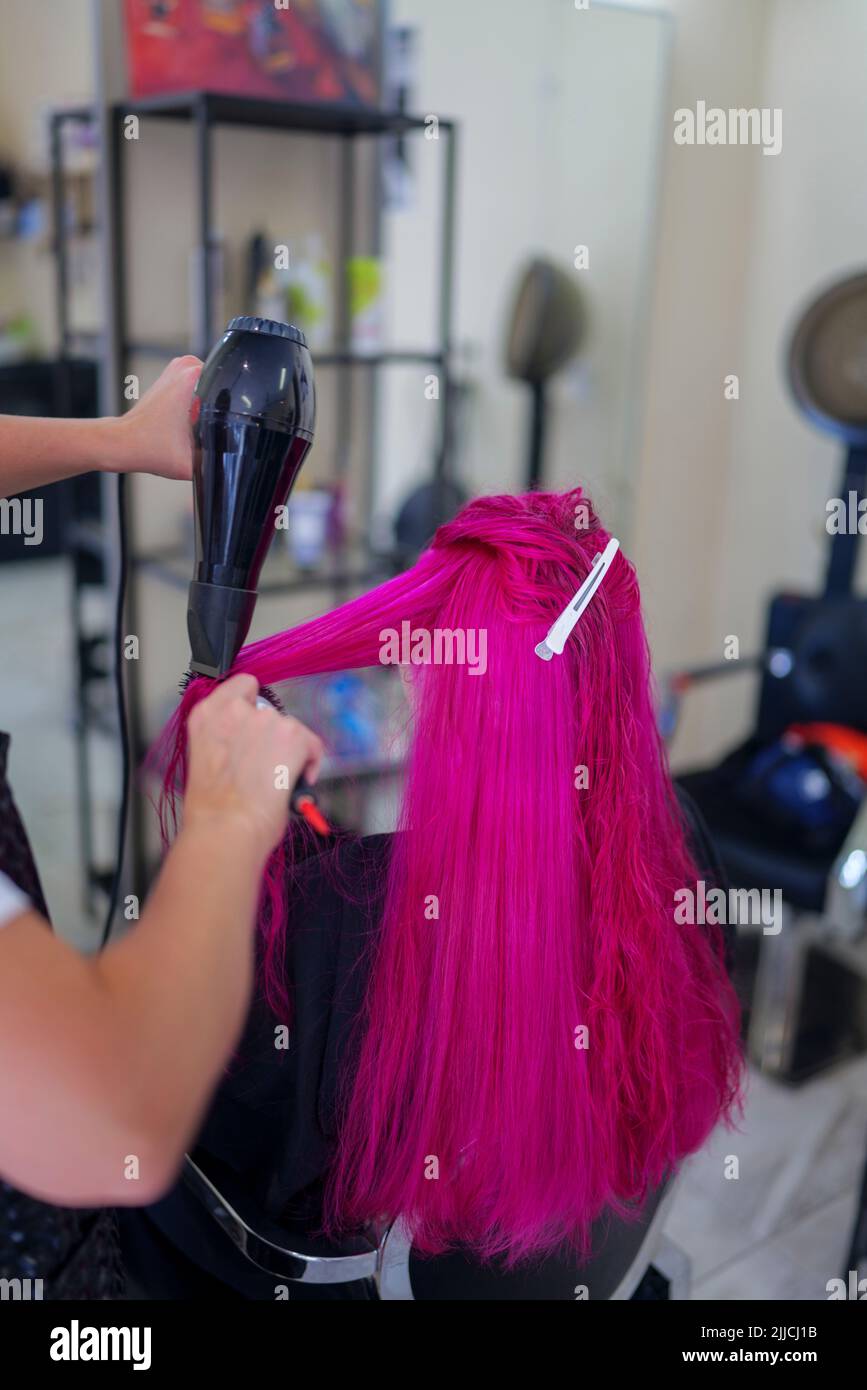 Haarfärbeverfahren im Salon. Mädchen trocknet und kämmt die Haare des Kunden nach dem Färben ihr Haar rosa. Stockfoto