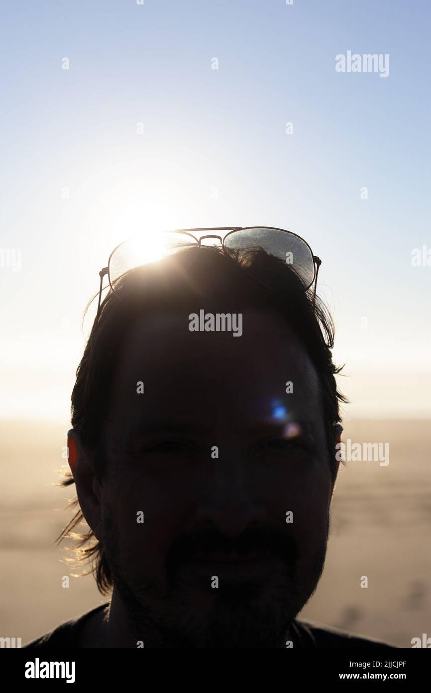 Ein Mann in Silhouette mit Sonnenbrille auf dem Kopf, mit Sonne, die durch die Linse scheint. Stockfoto