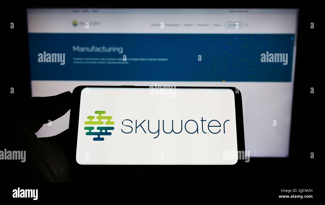 Person mit Mobiltelefon und Logo des US-Halbleiterunternehmens SkyWater Technology Inc. Auf dem Bildschirm vor der Webseite. Konzentrieren Sie sich auf die Telefonanzeige. Stockfoto