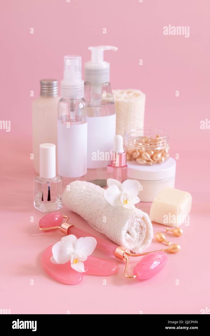 Natürliche Kosmetikgläser, Hautpflegeartikel und Rosenquarz-Massagegeräte mit weißer Orchideenblume auf hellrosa Nahaufnahme. Nachbau von Kosmetikprodukten. Ev Stockfoto
