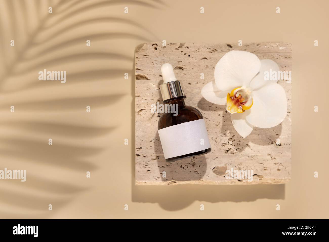 Braune Glasflasche auf Stein in der Nähe von weißen Orchideenblüten auf hellgelben Nahaufnahme, Etikett Mockup, Palmblatt harte Schatten. Hautpflege handgemachte Schönheit Stockfoto