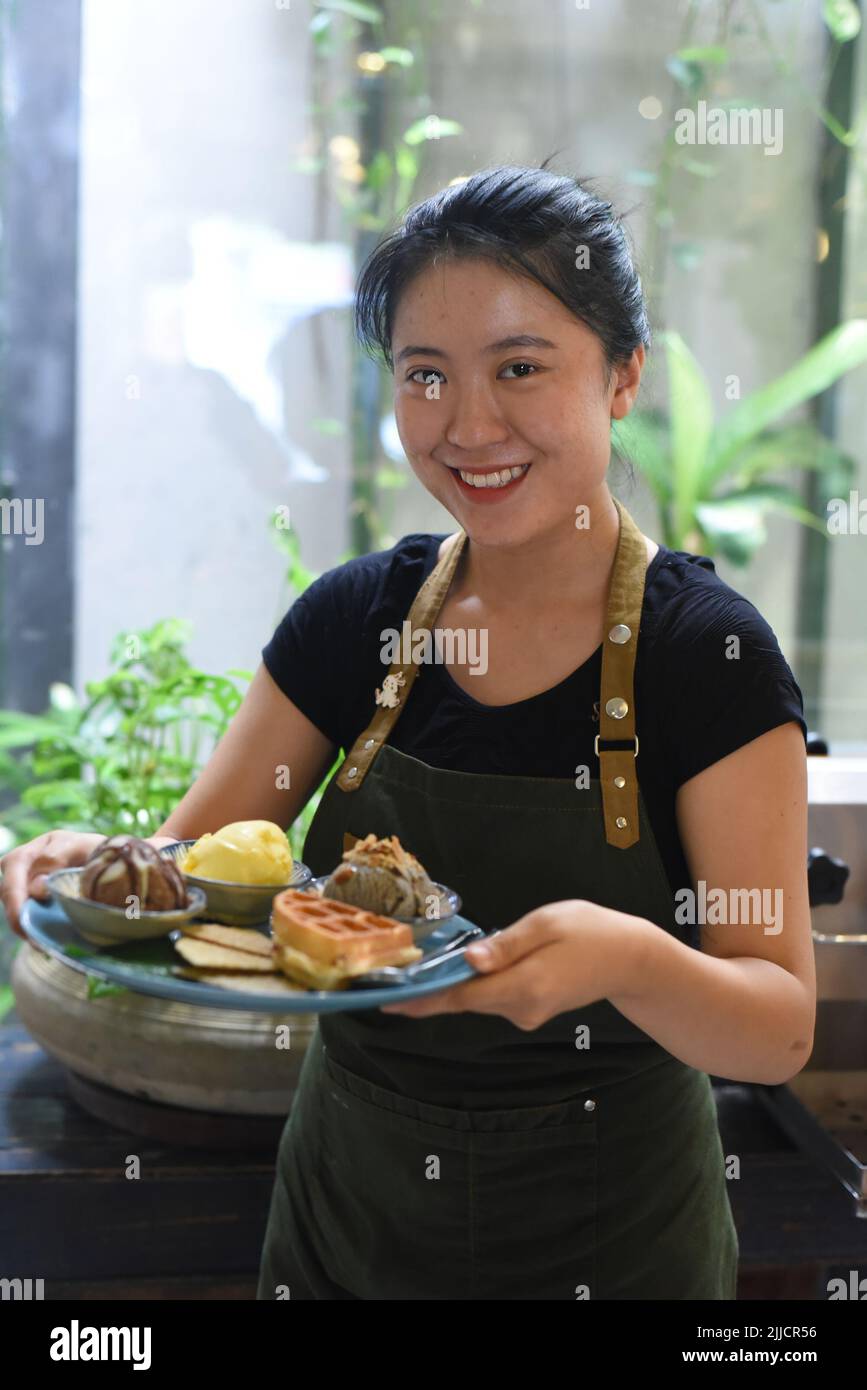 Vietnamesisches Mädchen, das in einem Café hausgemachtes Eis mit Waffeln serviert Stockfoto