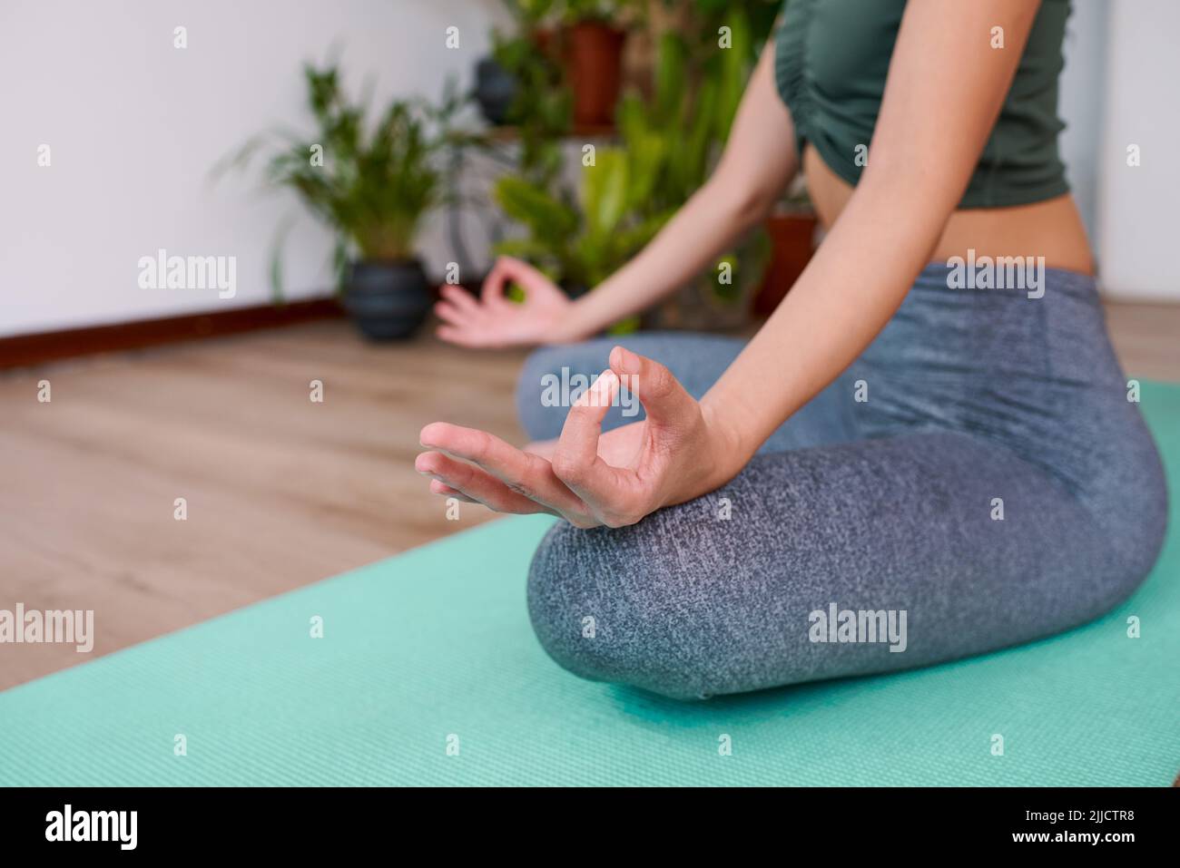 Eine Nahaufnahme einer Frau, die auf einer Yogamatte sitzt, mit den Händen in Gyan Mudra, die Finger berühren sich Stockfoto