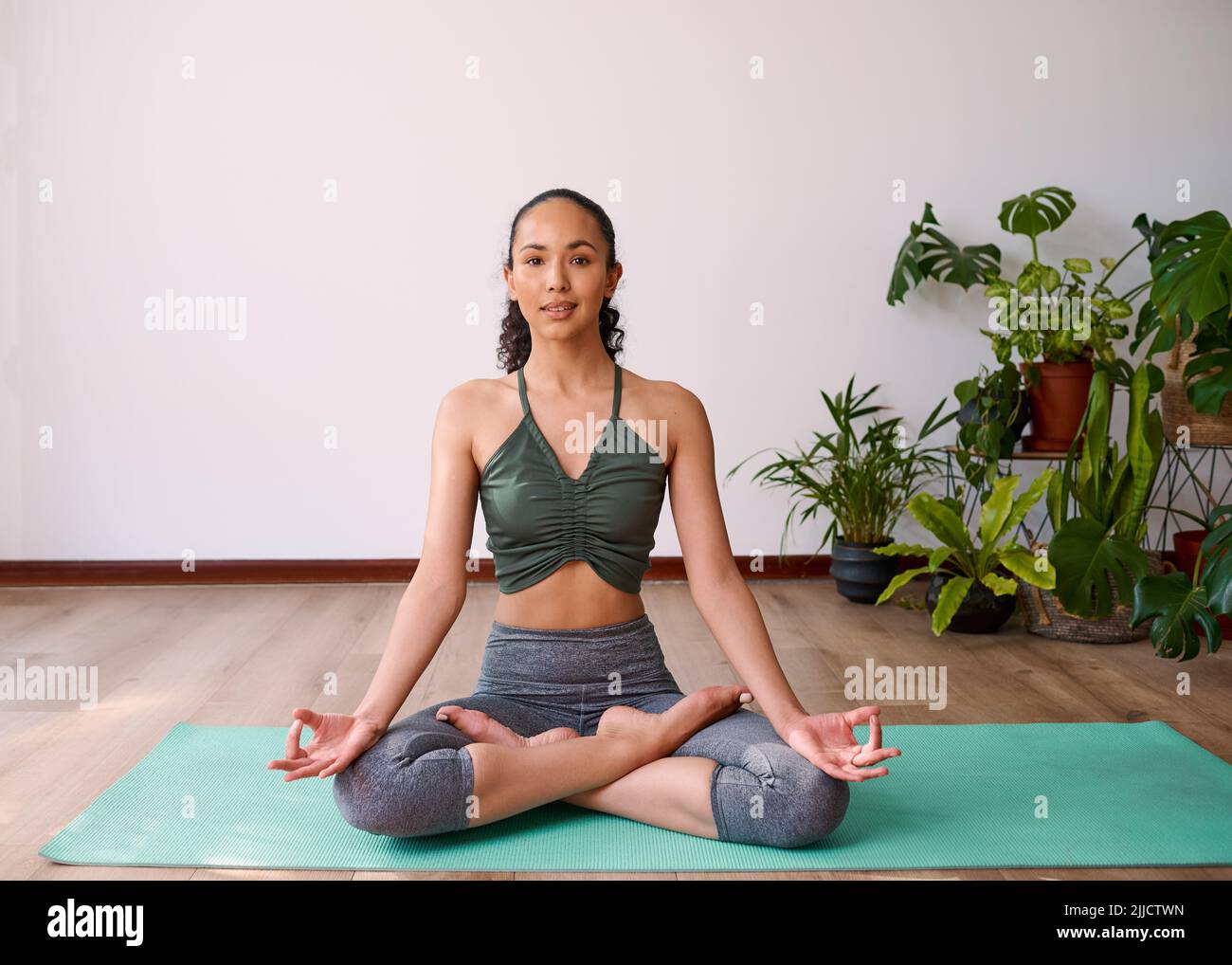 Eine attraktive, multiethnische Frau sitzt mit gekreuzten Beinen in der Sukhasana-Yoga-Pose Stockfoto