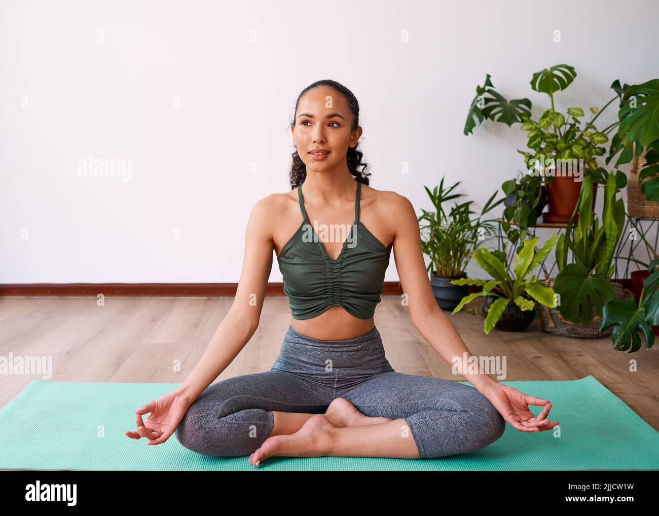 Eine attraktive, multiethnische Frau sitzt mit gekreuzten Beinen in der Sukhasana-Yoga-Pose Stockfoto