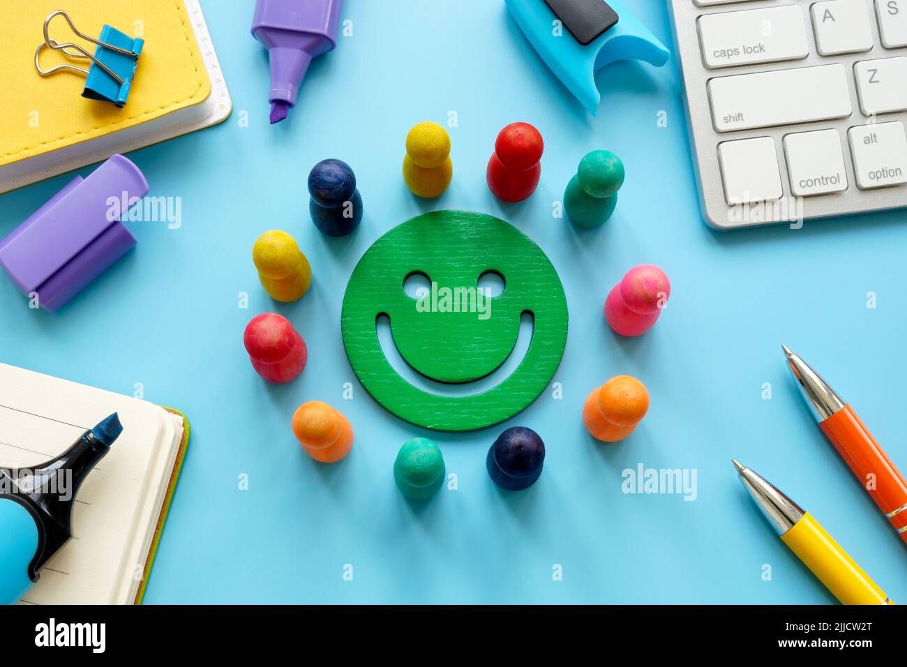 Smiley umgeben von farbigen Figuren auf dem Tisch. Konzept zur Mitarbeiterzufriedenheit. Stockfoto