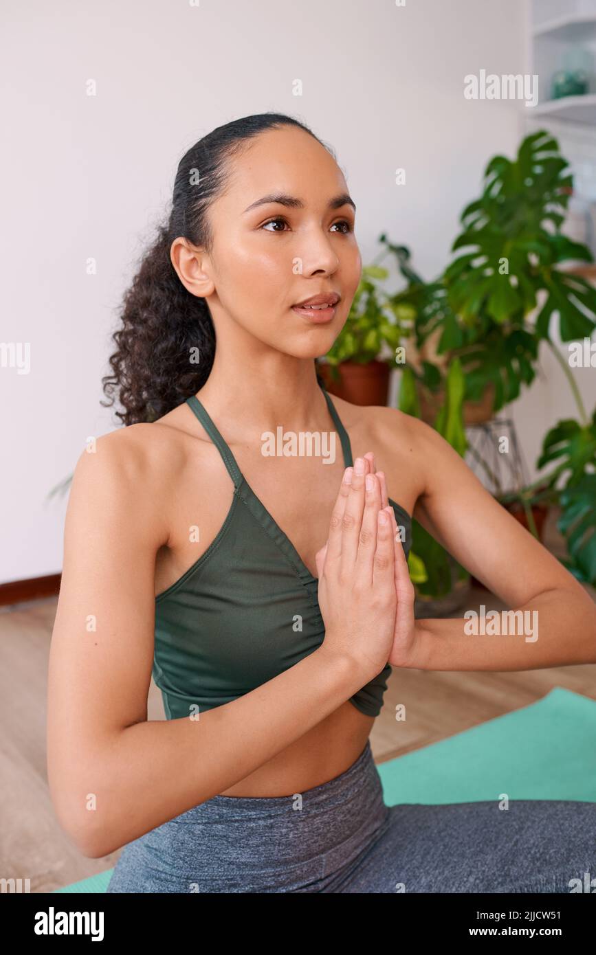 Eine junge, multirassische Frau sitzt in Gebetshaltung mit geöffneten Augen zu Hause Stockfoto