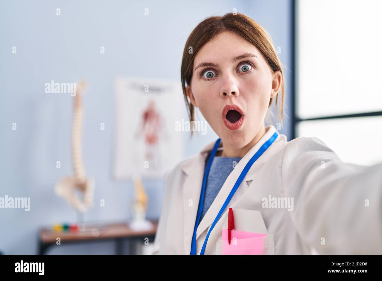 Junge Physiotherapeutin Frau, die in der Schmerzklinik arbeitet, erschreckte und staunte mit offenem Mund vor einem überraschenden, ungläubigen Gesicht Stockfoto