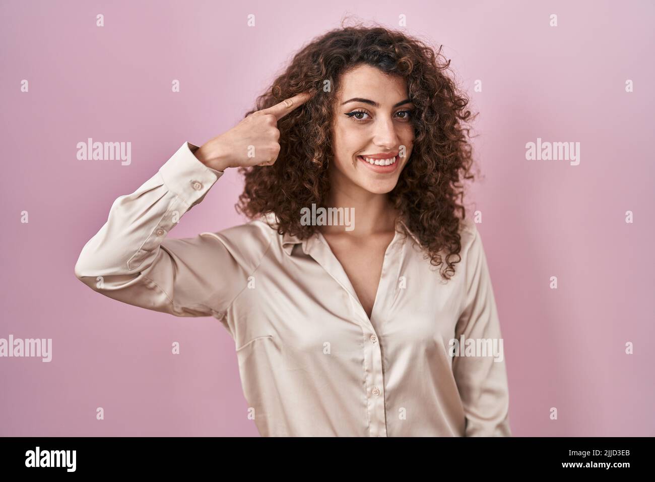 Hispanische Frau mit lockigem Haar, das über einem rosa Hintergrund