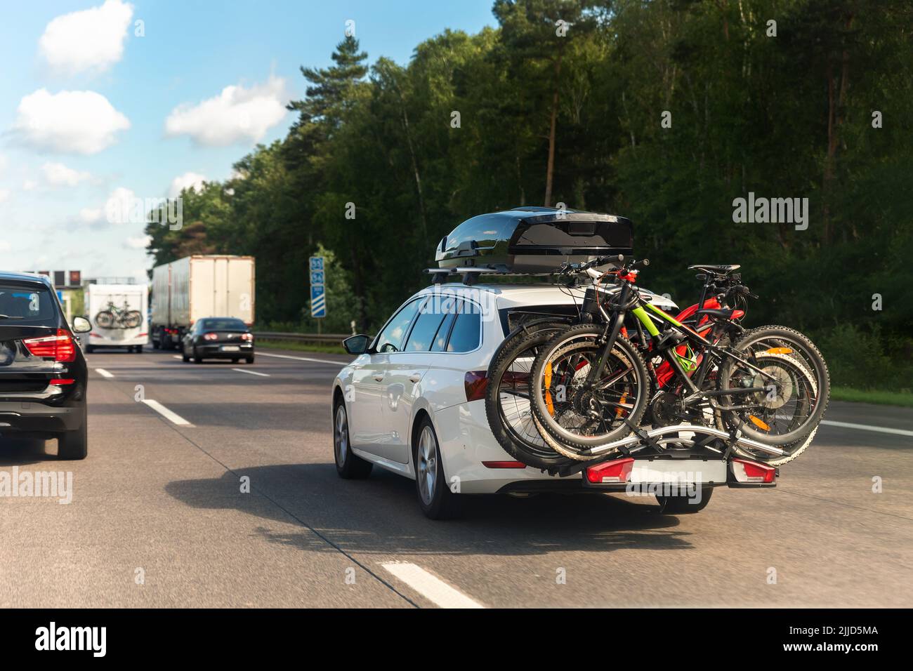Rückansicht moderner weißer Familienwaggon mit montiertem Dachkoffer-Kofferraum und Fahrradträger, der die europäische Autobahn gegen den blauen Himmel am Sommertag fährt Stockfoto