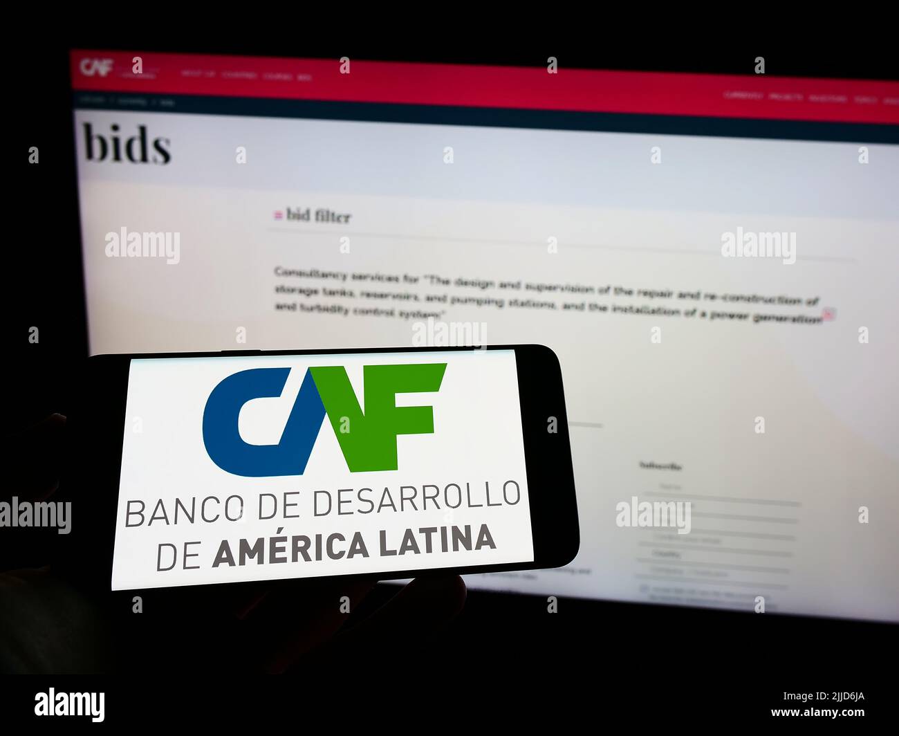 Person, die Mobiltelefon mit dem Logo von Corporacion Andina de Fomento (CAF) auf dem Bildschirm vor der Business-Webseite hält. Konzentrieren Sie sich auf die Telefonanzeige. Stockfoto
