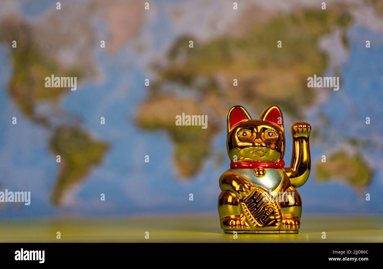 Maneki-neko ist ein Symbol für Glück in Japan, China und anderen asiatischen Ländern. Ein traditionelles Souvenir. Im Hintergrund ist eine Weltkarte. Stockfoto