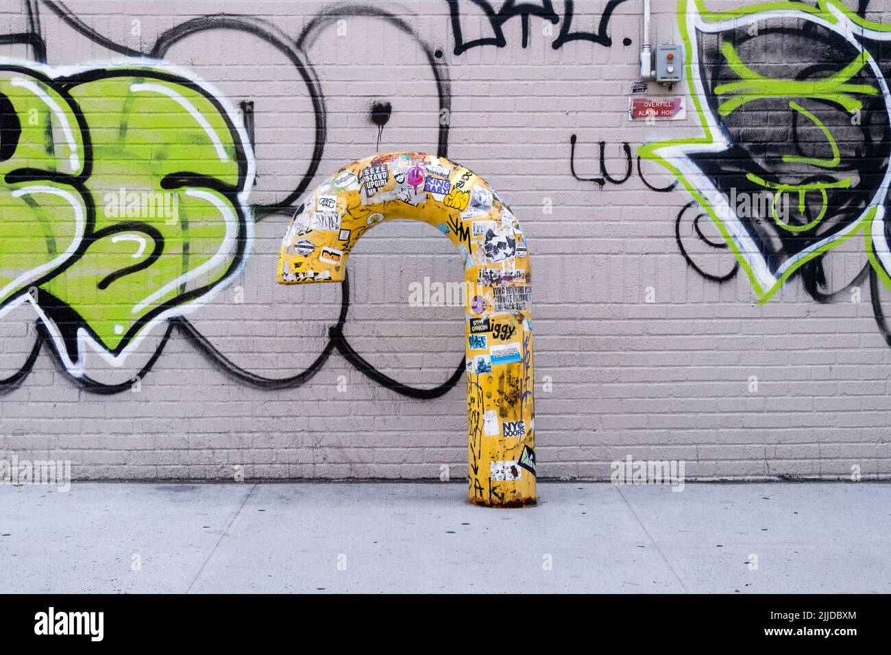 STADTLANDSCHAFT. Ein gelbes, kegelförmiges Rohr gegen eine mit Graffiti gefüllte Wand. Auf der Second Avenue in Greenwich Village. Wall. Stockfoto
