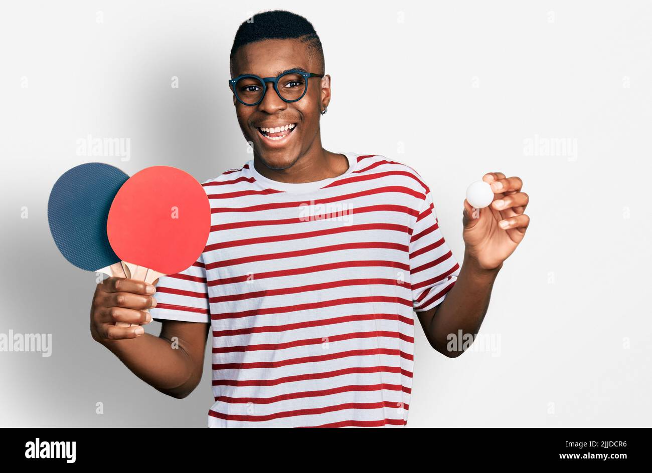 Junger afroamerikanischer Mann mit roten Ping-Pong-Schlägern und Ball feiert verrückt und erstaunt über den Erfolg mit offenen Augen schreiend aufgeregt. Stockfoto