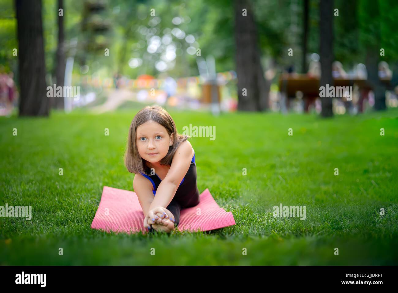 Ein kleines Mädchen im Park macht Yoga, dehnt sich an ihrem Bein. Ein Mädchen sitzt auf einem Garn Stockfoto