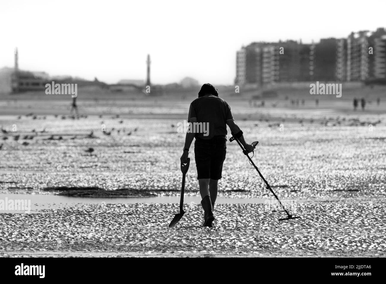 Mann mit Metalldetektor, der an einem frühen Morgen im Sommer während der Ferienzeit am Sandstrand entlang der Nordseeküste strandkämmt Stockfoto
