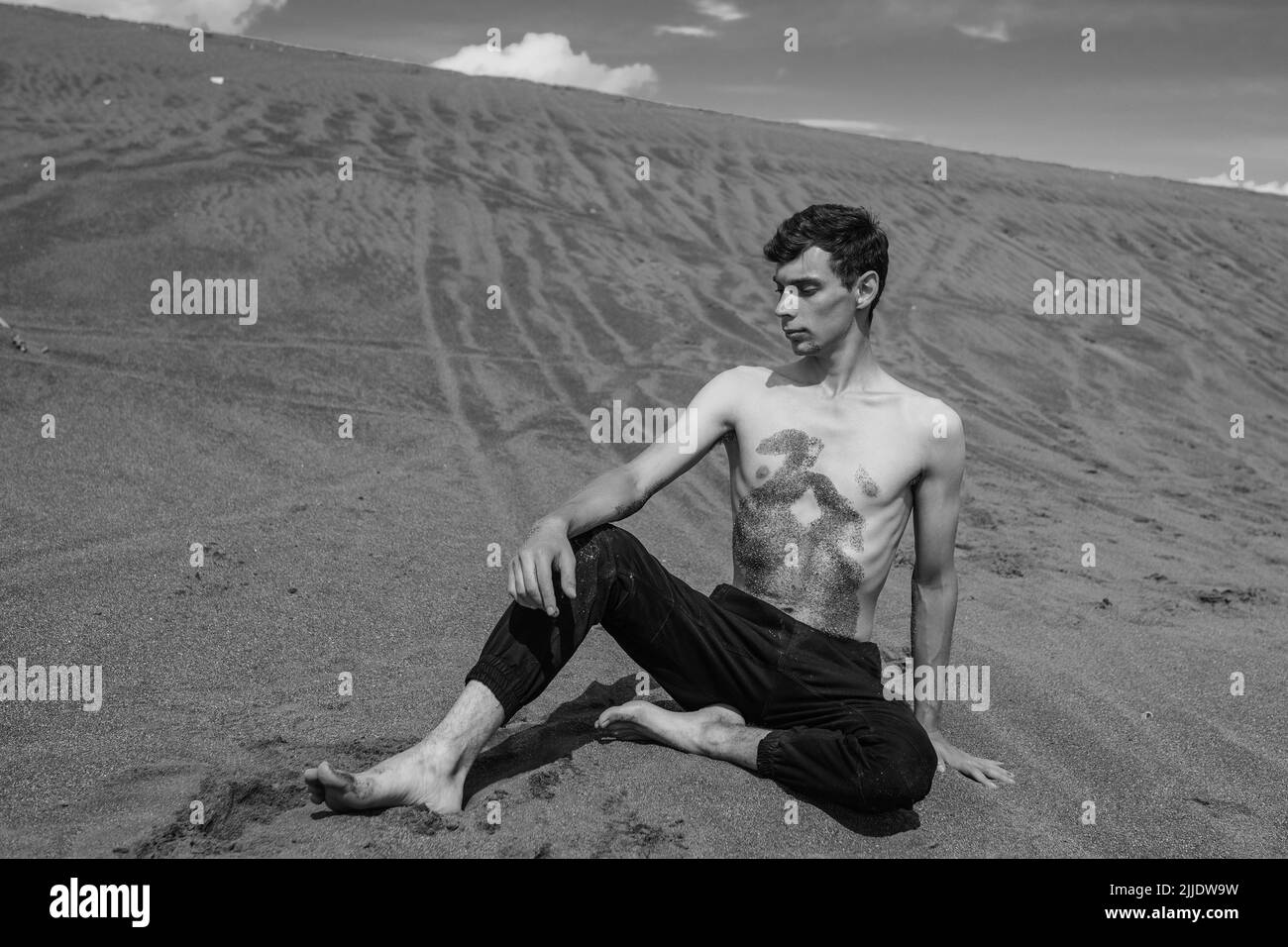 Mann, der auf dem Sand in der sandigen Wüste sitzt. Schwarz und Weiß Stockfoto