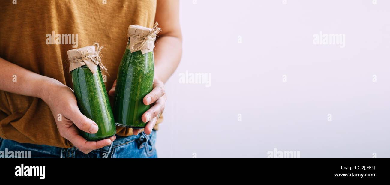 Weibliche Hände halten Flaschen frisch zubereiteter grüner Smoothies, Kopierraum. Lieferung von frischen Getränken Stockfoto