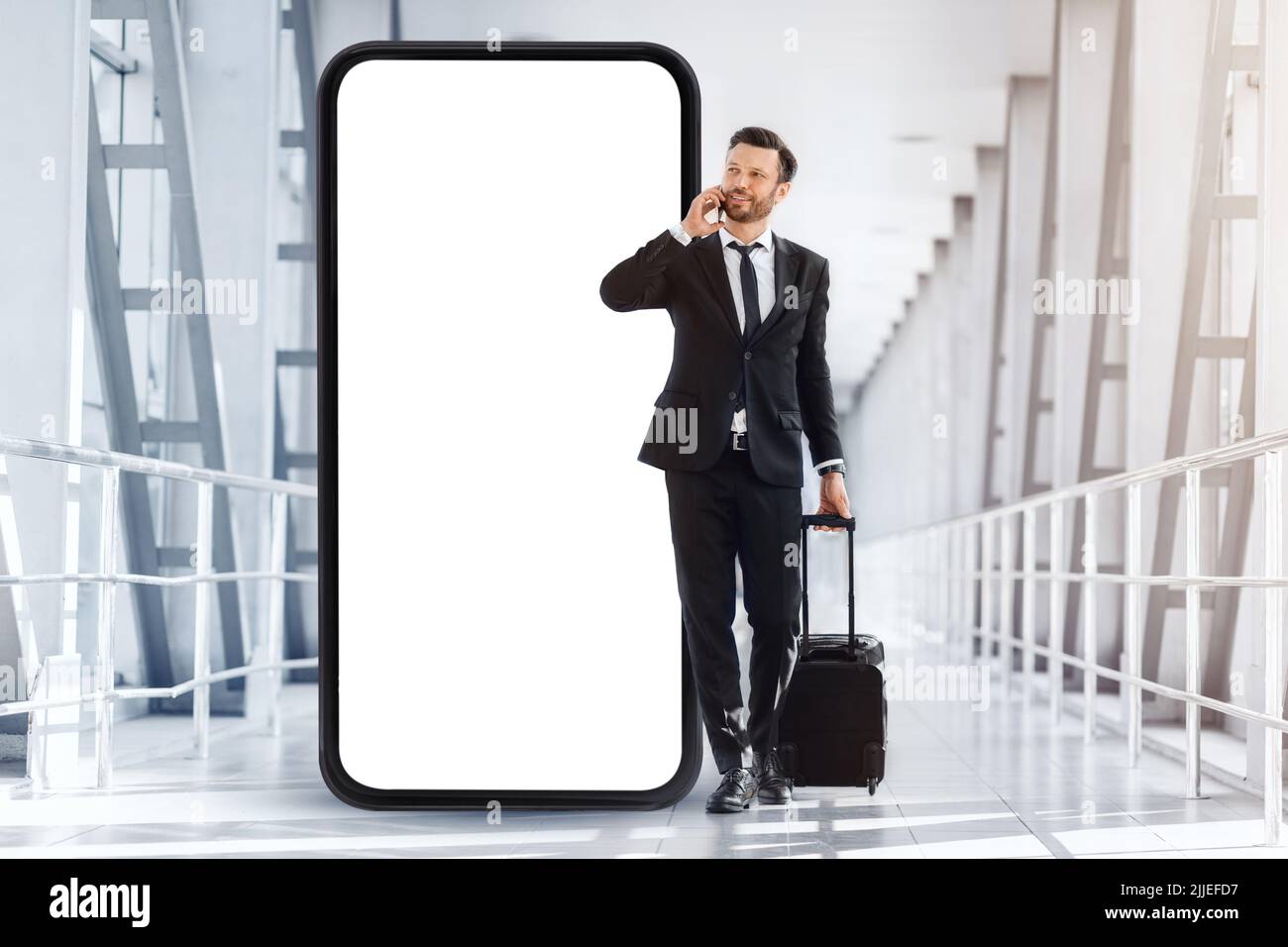 Wohlhabender Unternehmer mit Koffer, der am Flughafen läuft und telefoniert Stockfoto