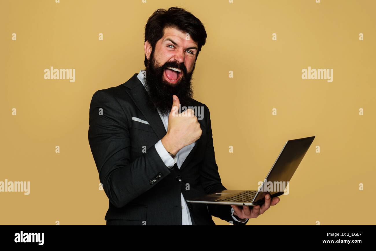 Ein glücklicher Geschäftsmann mit Laptop zeigt den Daumen nach oben. Bärtiger Mann im Anzug mit Notebook im Büro. Stockfoto