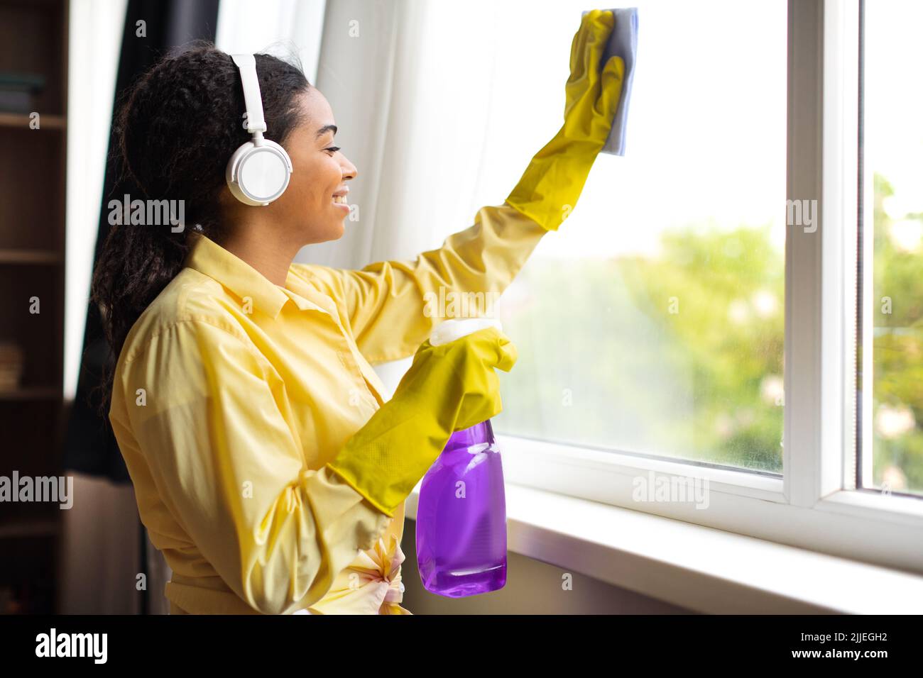 African American Frau Reinigung Fenster Glas Mit Waschmittel Spray Indoor Stockfoto