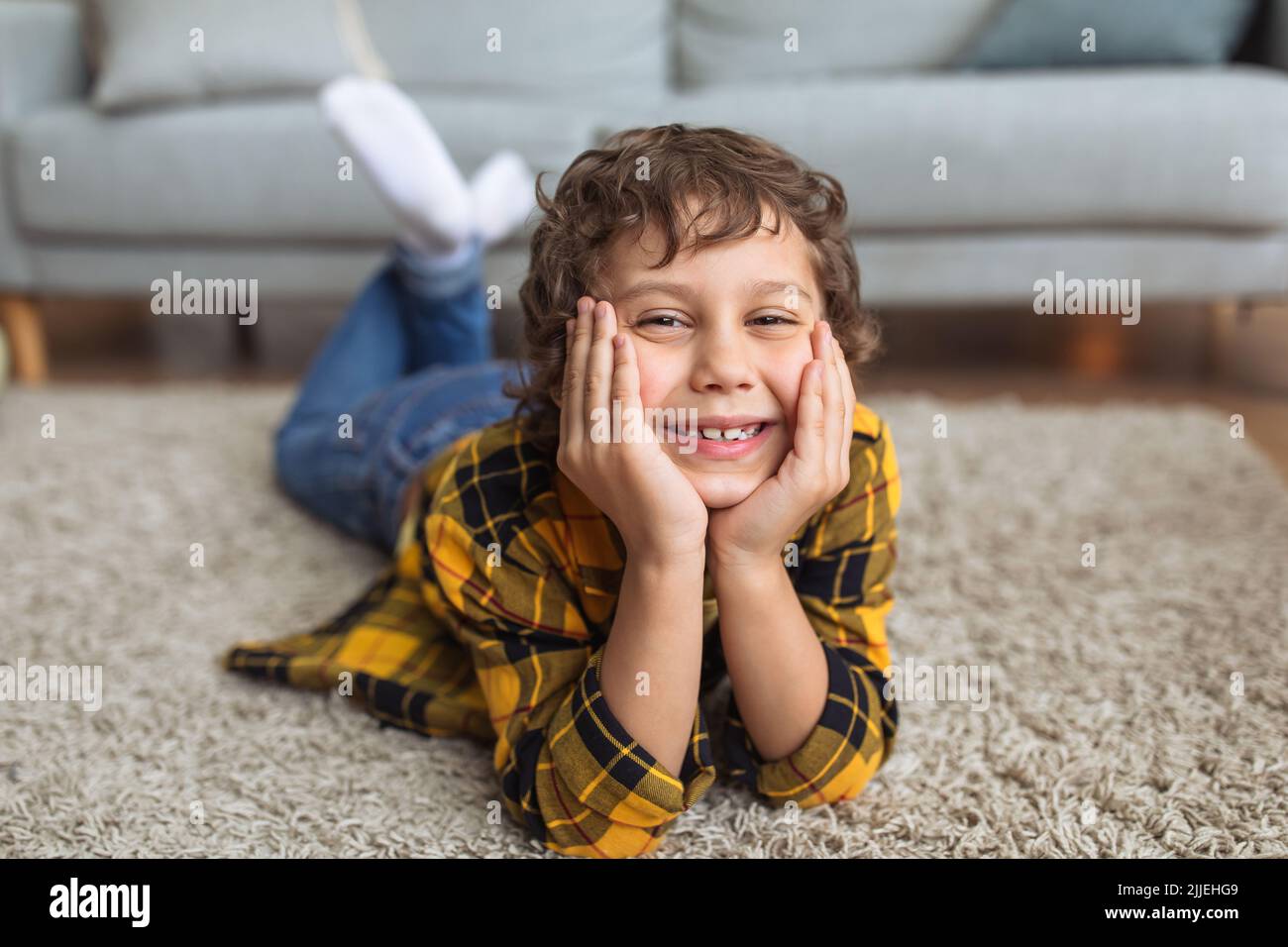 Frohe Kindheit. Nahaufnahme eines fröhlichen kleinen Jungen, der lächelt und zu Hause auf dem Boden liegt Stockfoto