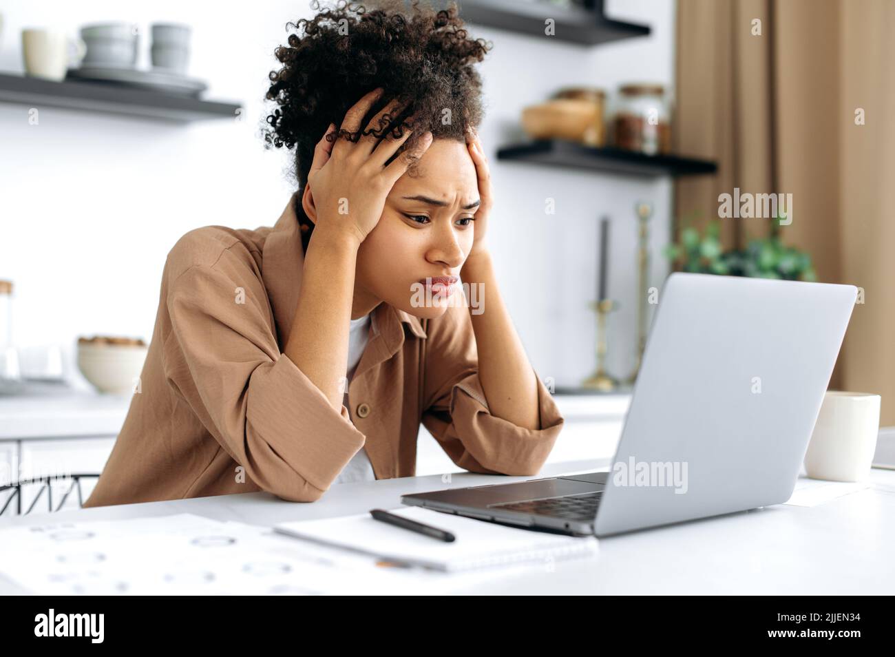 Verzweifelt besorgt traurig afroamerikanische junge Frau, mit Laptop für die Arbeit oder Studium von zu Hause aus, sitzen in der Küche, frustriert Blick auf den Bildschirm, gescheitert Projekt, bekam finanziellen Verlust, Arbeitsplatz Downgrade Stockfoto