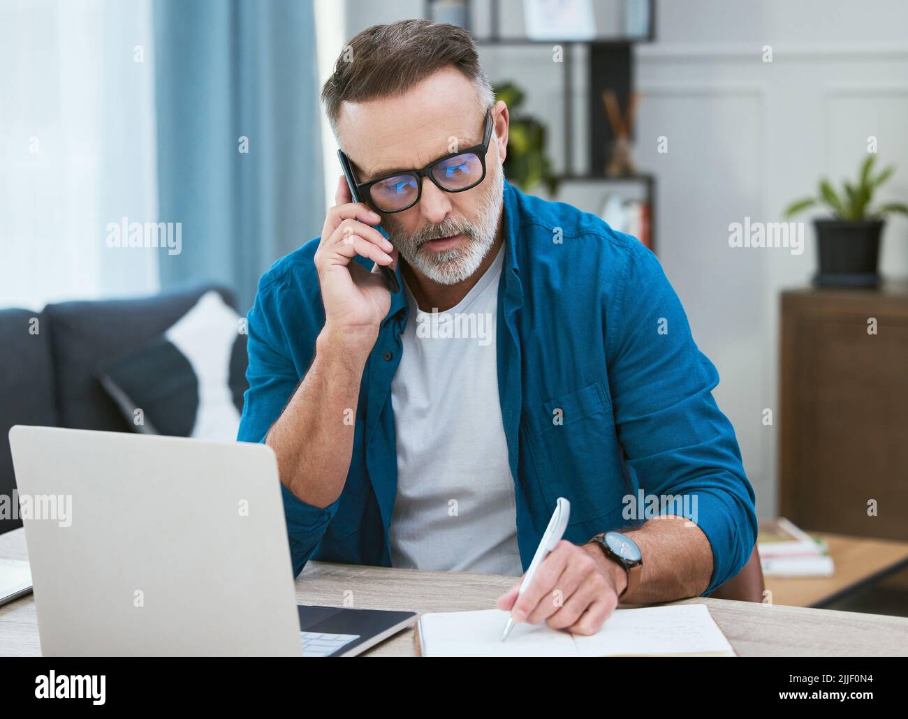 Wiederholen Sie das langsam für mich. Ein reifer Geschäftsmann, der von zu Hause aus arbeitet, während er einen Anruf macht. Stockfoto