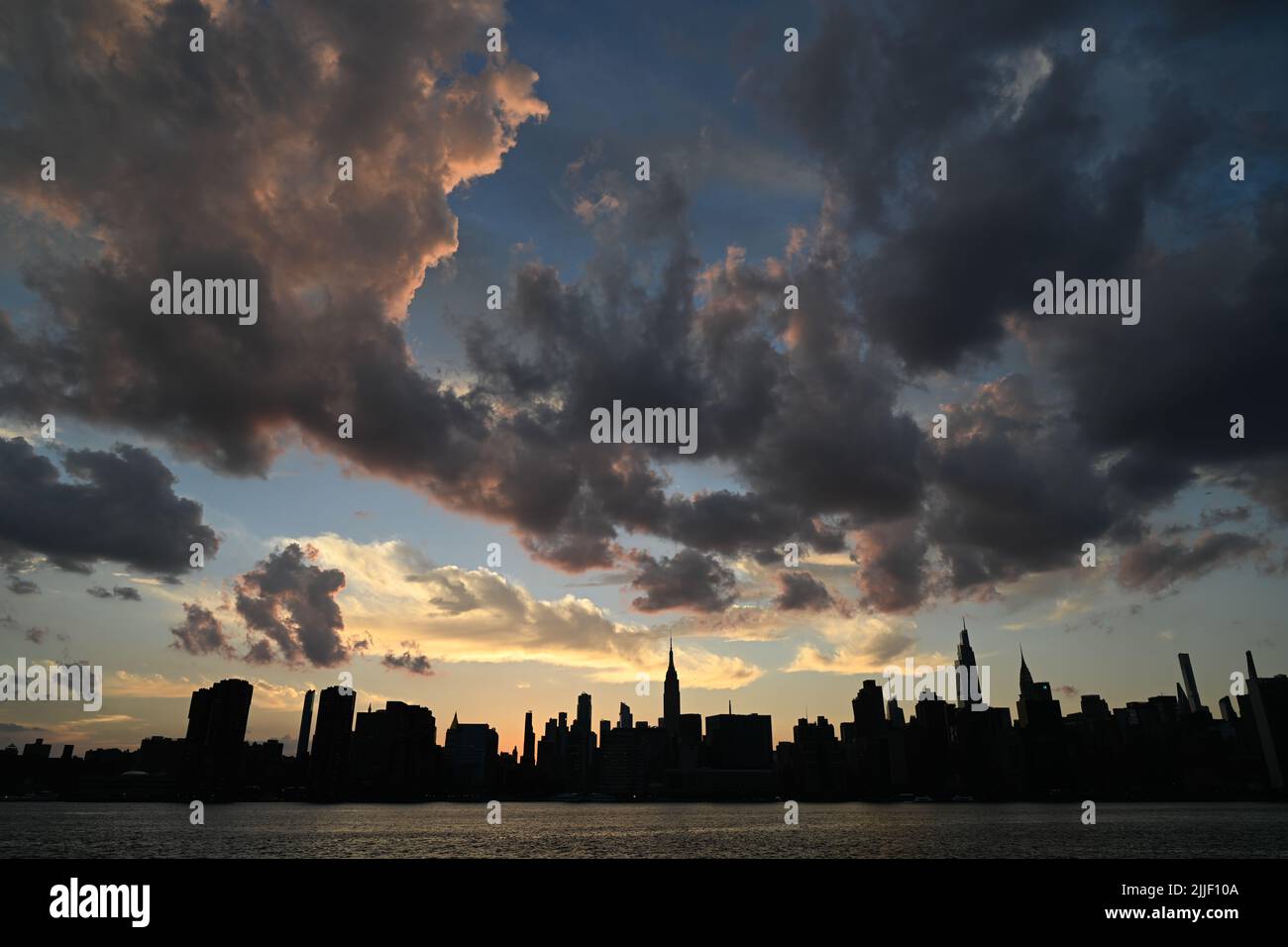 Die Sonne untergeht hinter der Skyline von Manhattan, von der Uferpromenade aus gesehen, im Stadtteil Greenpoint in Brooklyn, New York. Stockfoto