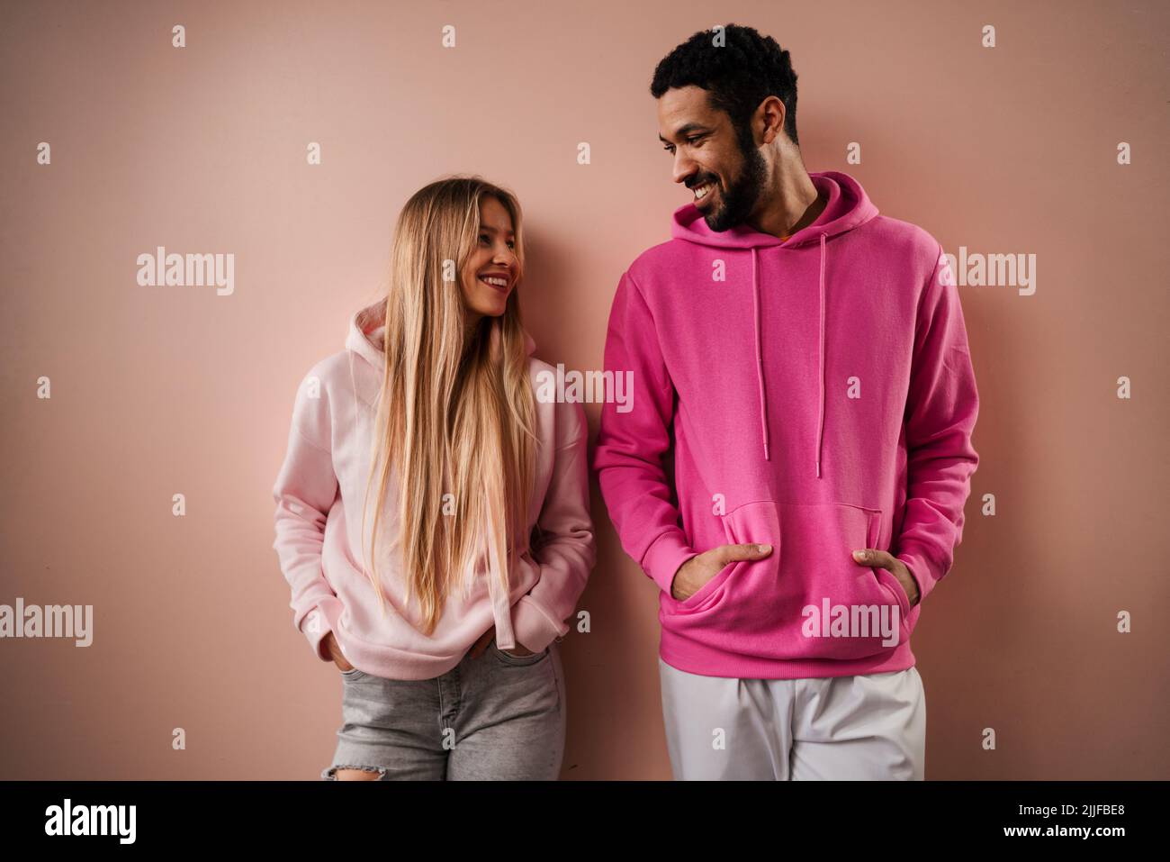 Romantisches Modestudio-Portrait eines jungen Biracial-Paares verliebt in Hoodie posiert auf rosa Hintergrund. Stockfoto