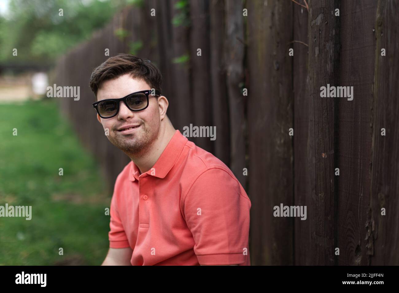 Porträt eines glücklichen jungen Mannes mit Down-Syndrom, der im Park steht und eine Sonnenbrille trägt Stockfoto