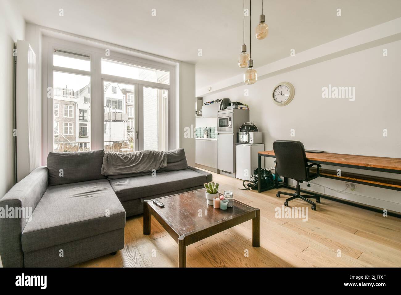 Einfache offene Küche mit weißen Schränken und Wohnzimmer mit grauem Sofa bei Tageslicht Stockfoto