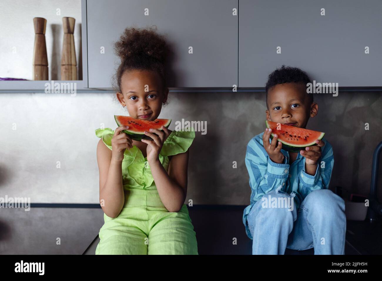 Multirassische Kinder essen Melone in der Küche an heißen sonnigen Tagen. Stockfoto
