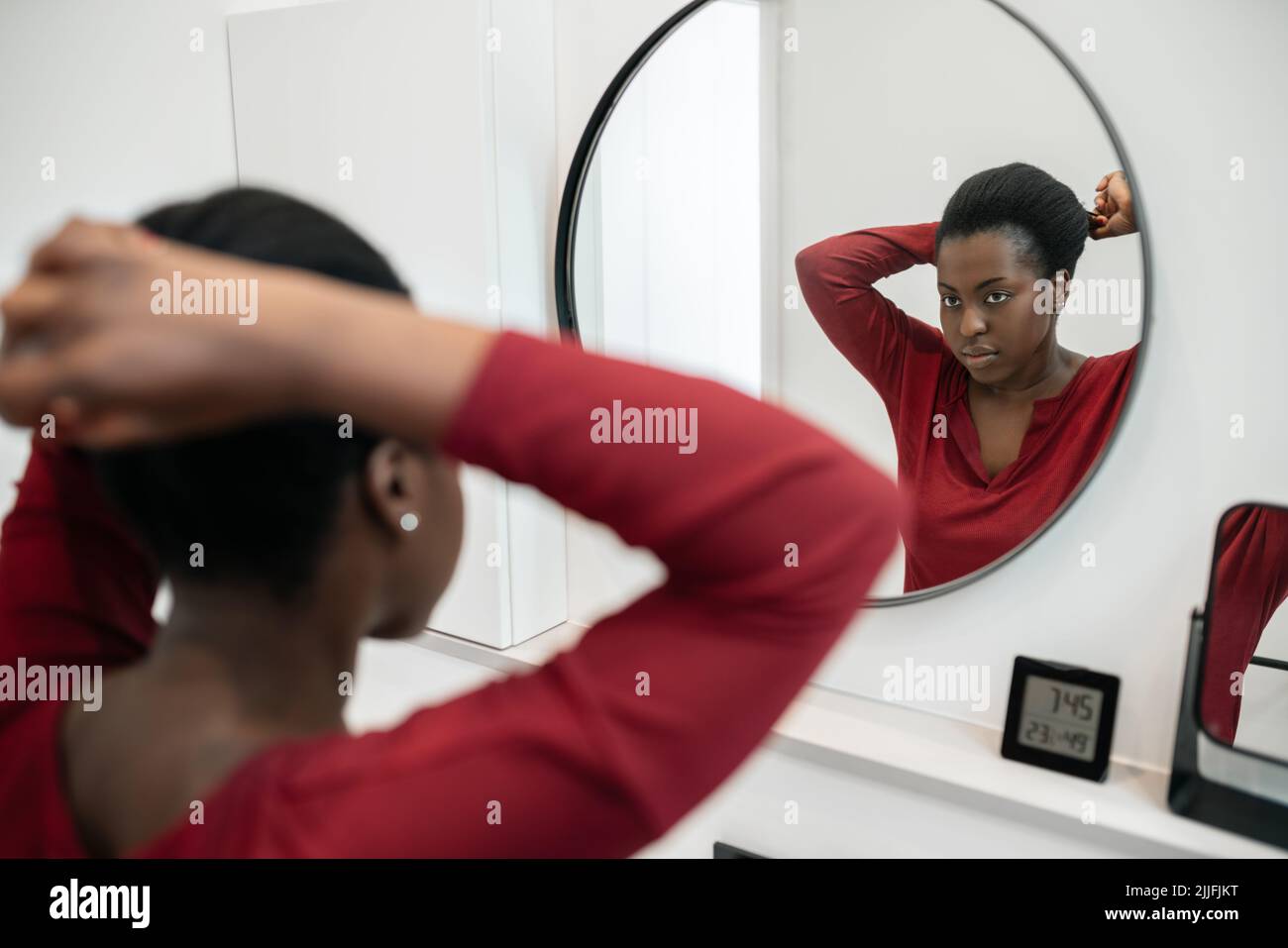 Trauerroutine der schwarzen afrikanischen Frau, die ihre Haare fixiert und in den Badezimmerspiegel schaut. Haarstyling und Vorbereitung Stockfoto