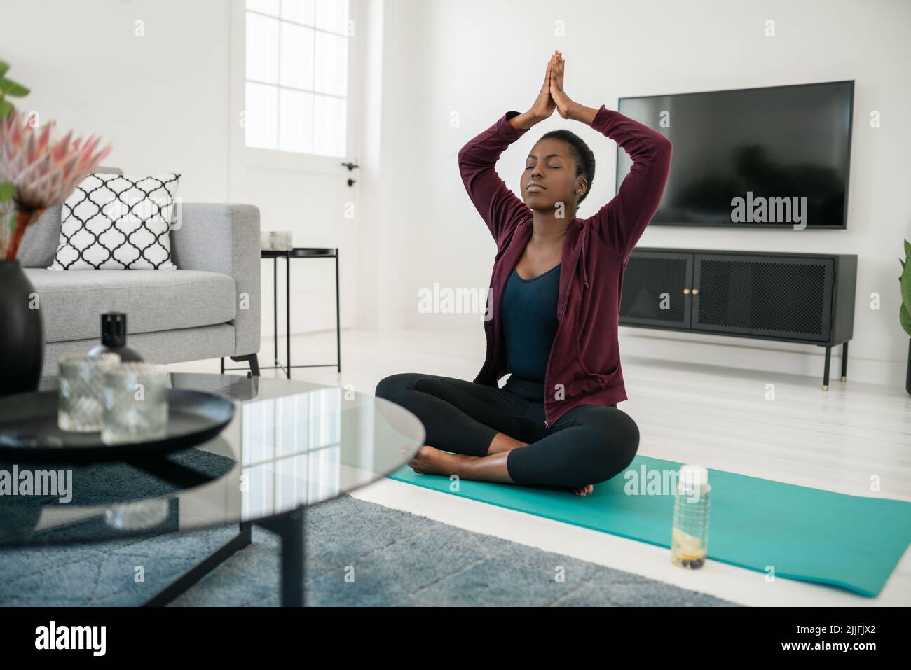 Schwarze afrikanische Frau sitzt in Yoga-Pose auf Matte im Wohnzimmer, Stretching und Meditation zu Hause trainieren Stockfoto