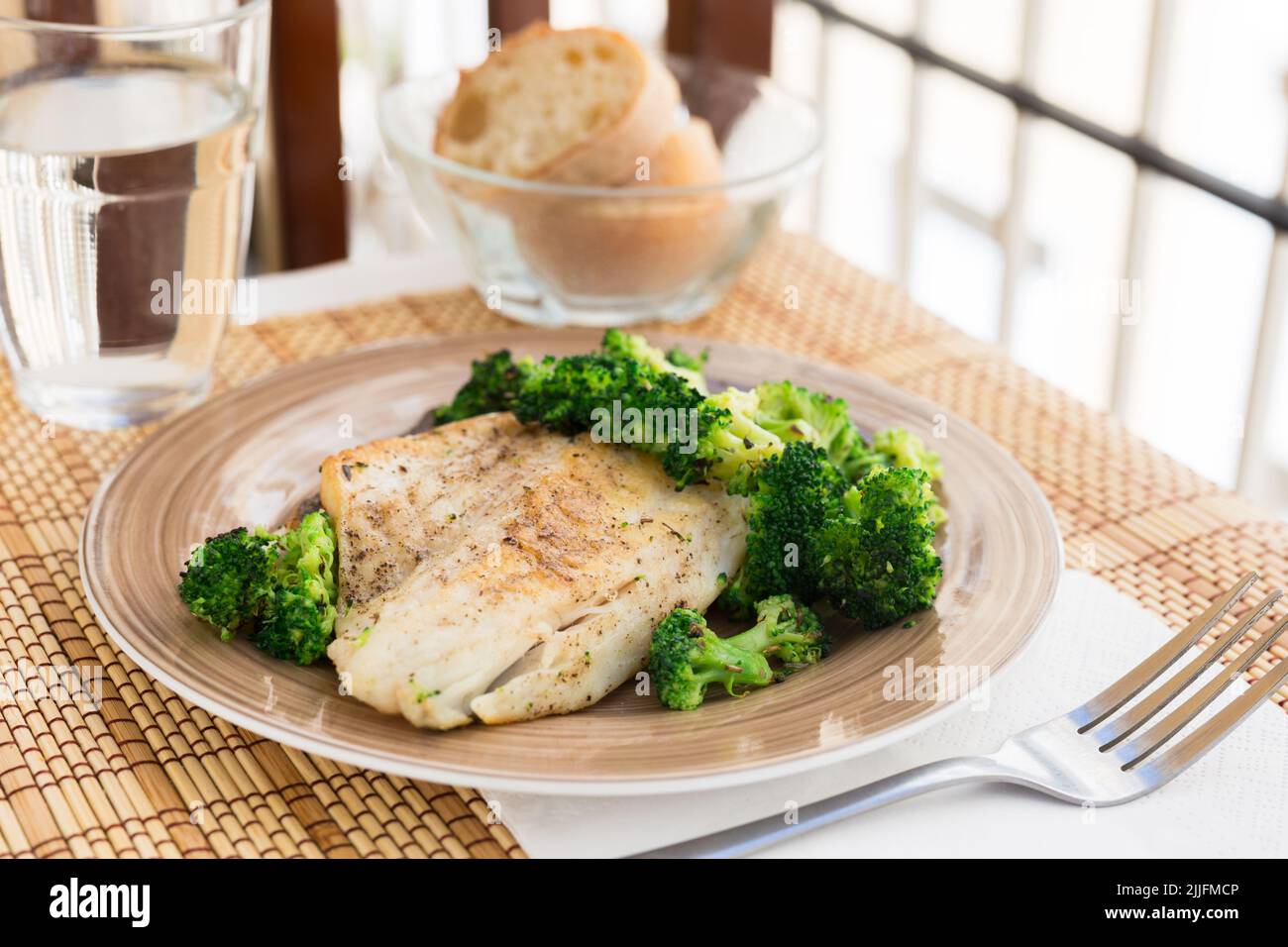 Gebratenes Seebarschfilet mit Brokkoli-Garnitur auf schwarzem warmen Steinteller Stockfoto