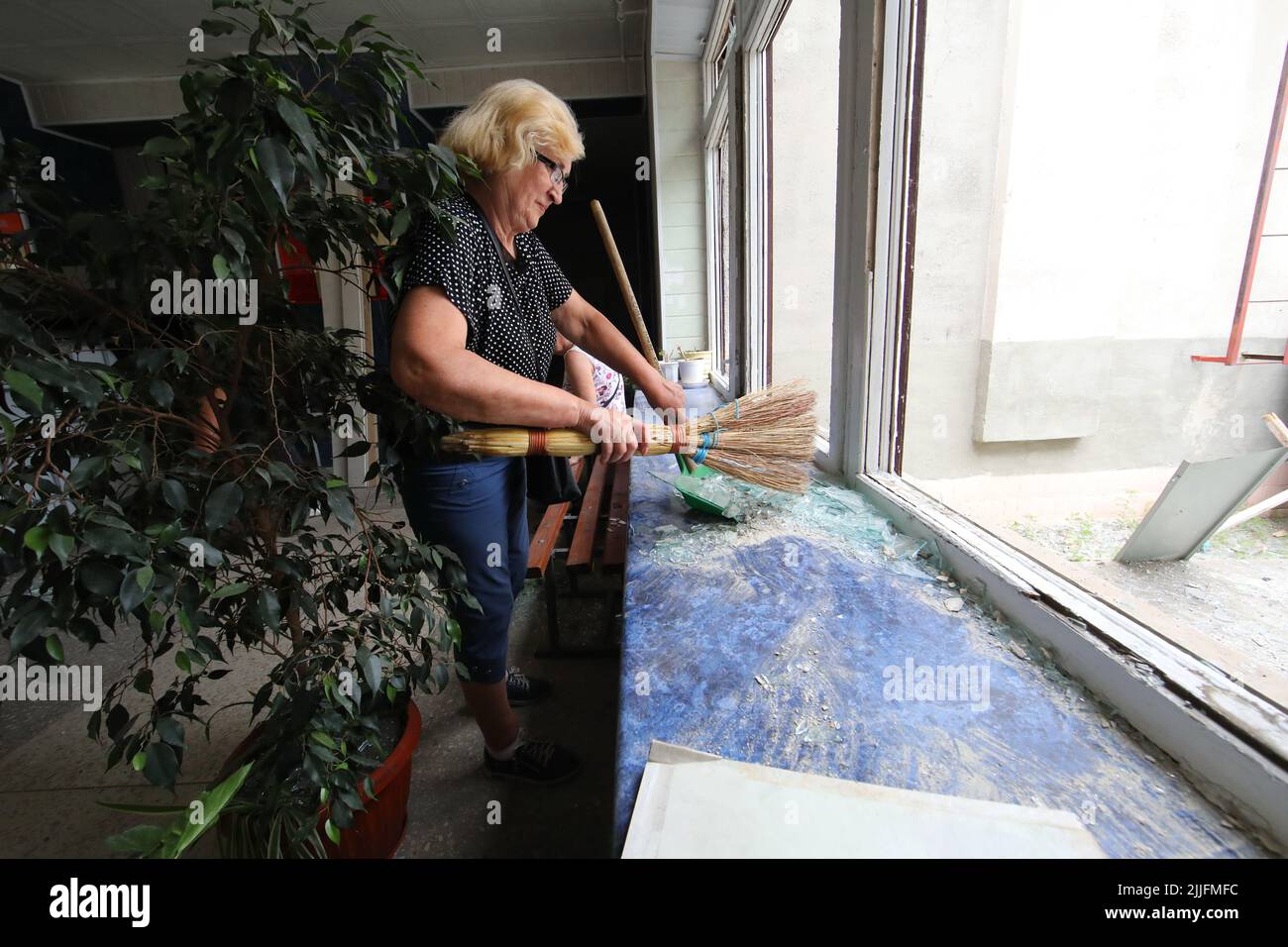 REGION CHARKIW, UKRAINE - 25. JULI 2022 - Eine Frau fegt Glasscherben aus einer Fensterbank in einer Schule, die durch den Beschuss russischer Truppen, Tschuhuiv, ruiniert wurde Stockfoto