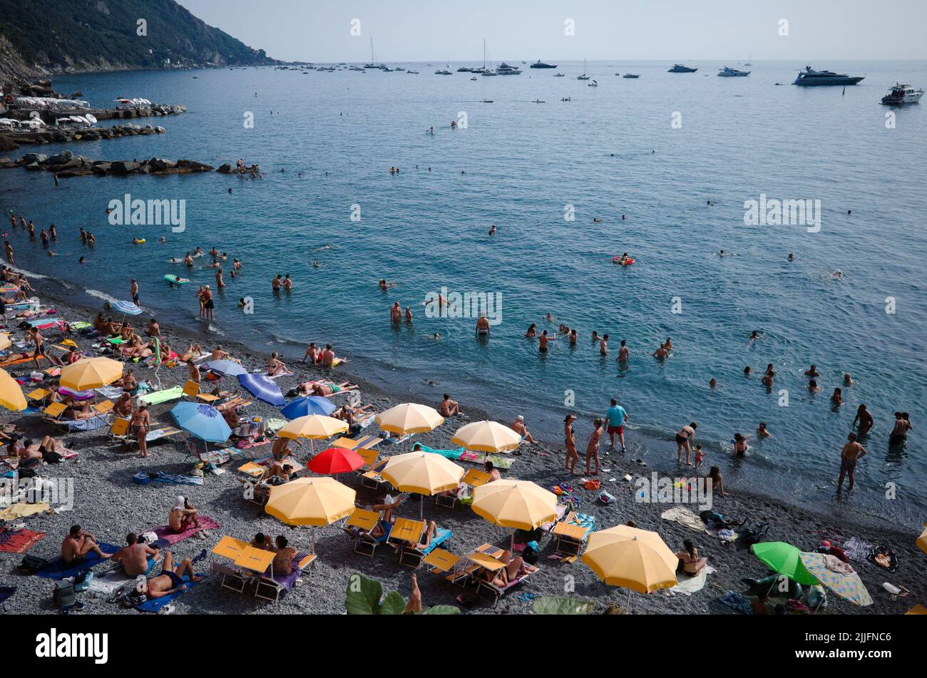 Camogli, Ligurien, Italien - Juni 2022: Menschen liegen auf Liegestühlen unter Sonnenschirmen, sonnen sich und schwimmen im Mittelmeer an der Küste von Riviere Stockfoto
