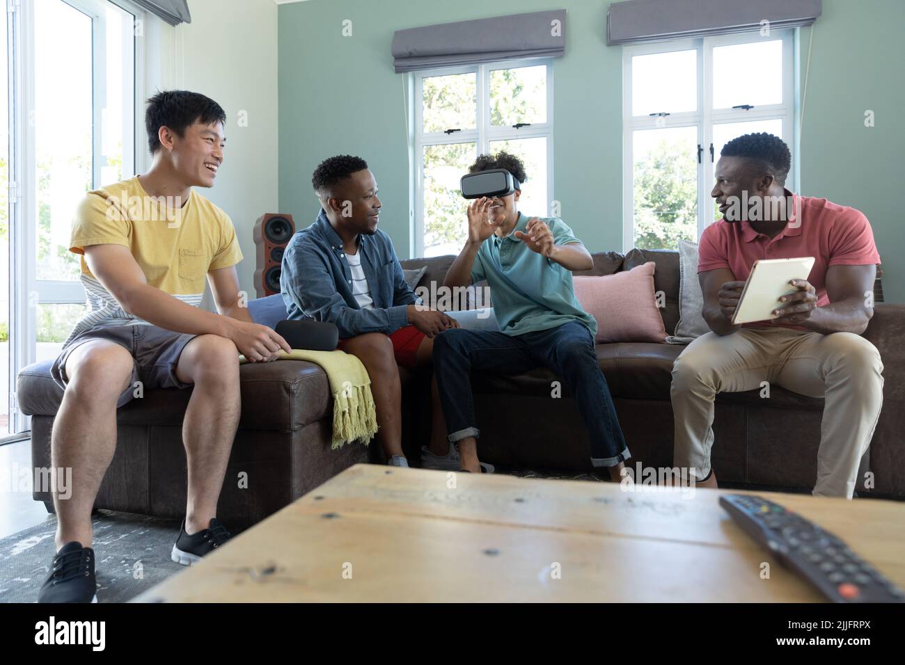 Multirassischer Mann mit digitalem pc und Freund, der zu Hause über ein Virtual-Reality-Headset auf dem Sofa spielt Stockfoto