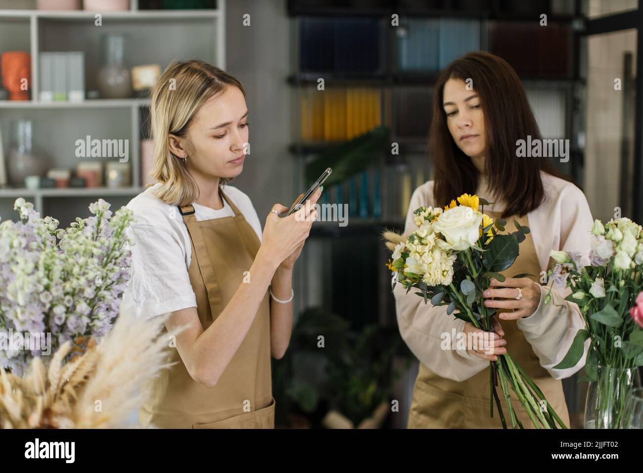 Zwei Floristinnen machen Mode modernen Blumenstrauß aus verschiedenen Blumen auf der Theke und fotografieren für Social Media. Meisterkurs. Geschenk für Braut auf Hochzeit, Mutter, Frauentag. Stockfoto