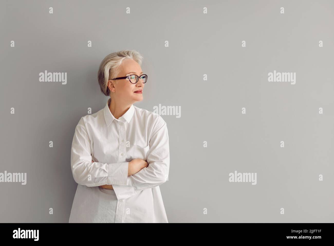 Porträt einer selbstbewussten reifen Geschäftsfrau in Hemd und Brille, die an der grauen Copy Space Wand steht Stockfoto